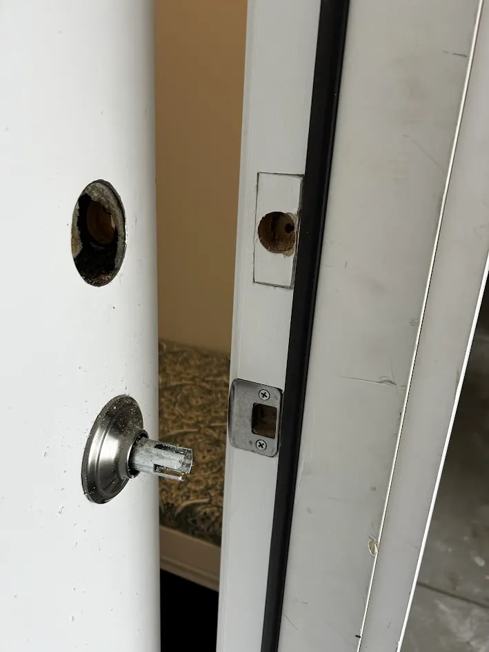 The bored hole in the door edge with the latch plate and the frame strike opening visible on the ajar door