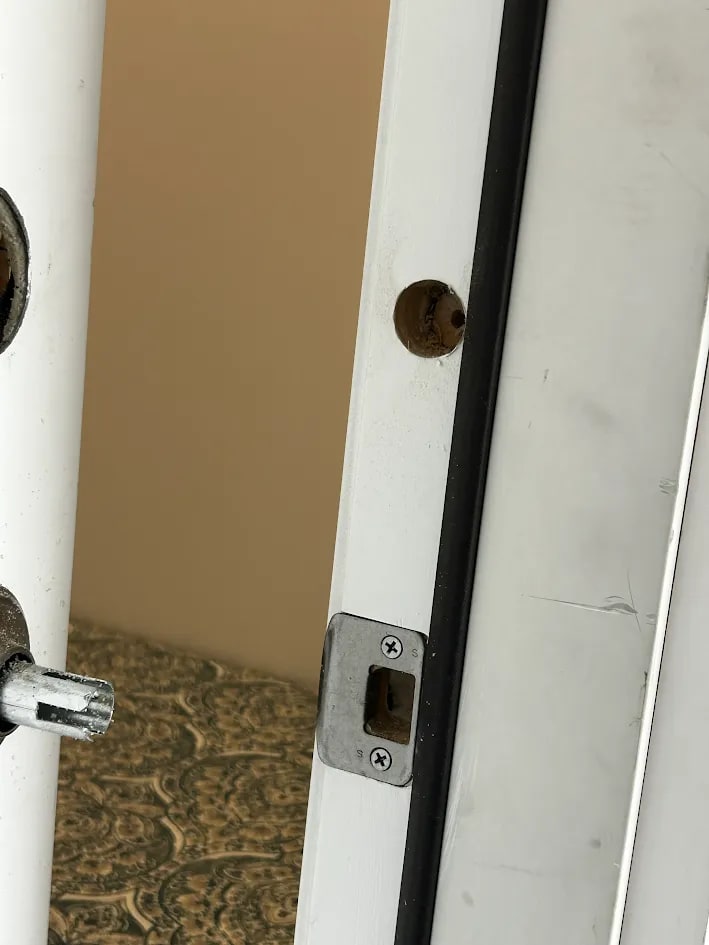 The edge of the door showing the bored hole for the deadbolt bolt and the latch, with the painted door frame beyond