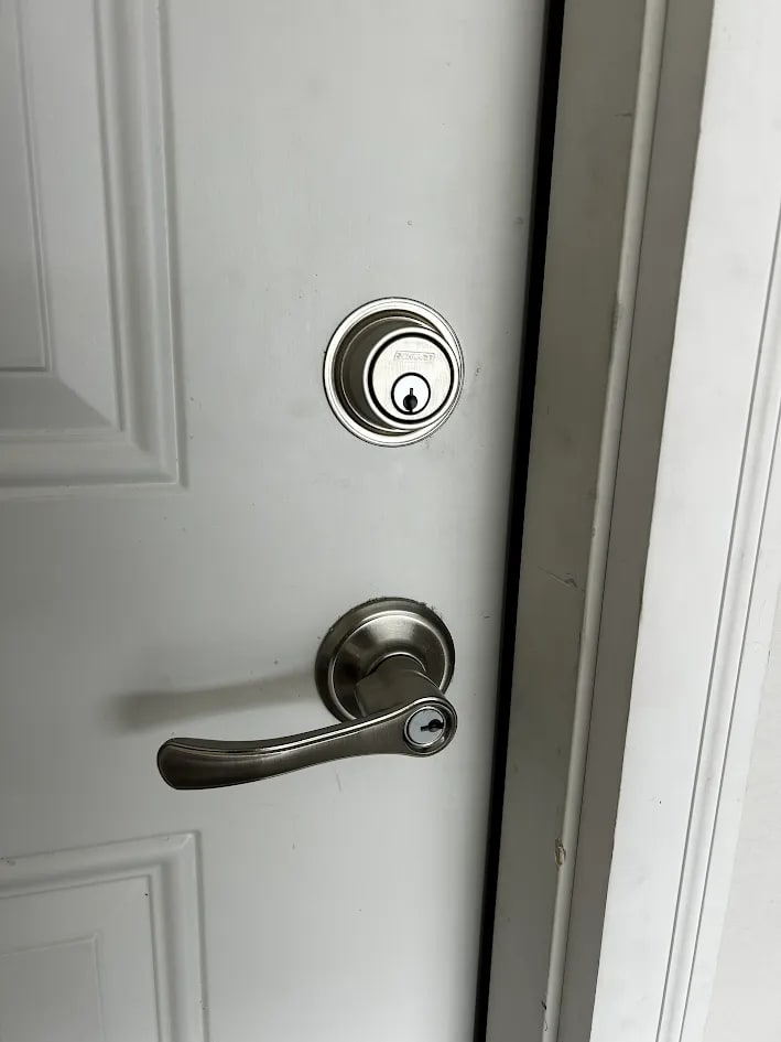 A finished white paneled door with a brushed steel deadbolt above a matching keyed lever handle