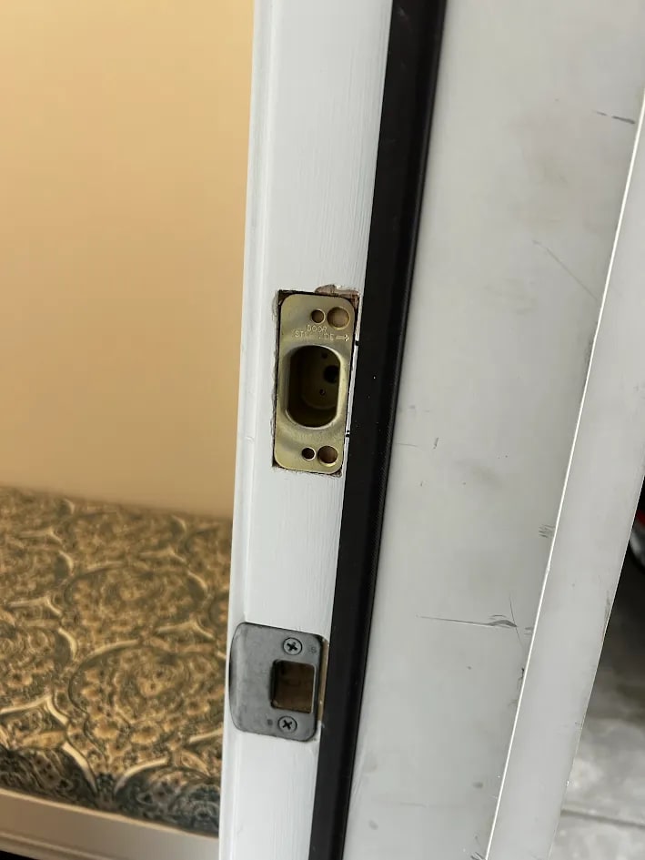 A strike plate set into a white painted door frame above a square latch plate, with the bolt opening cut into the frame