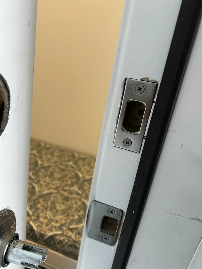 A steel strike plate screwed to the white painted door frame above a square latch plate