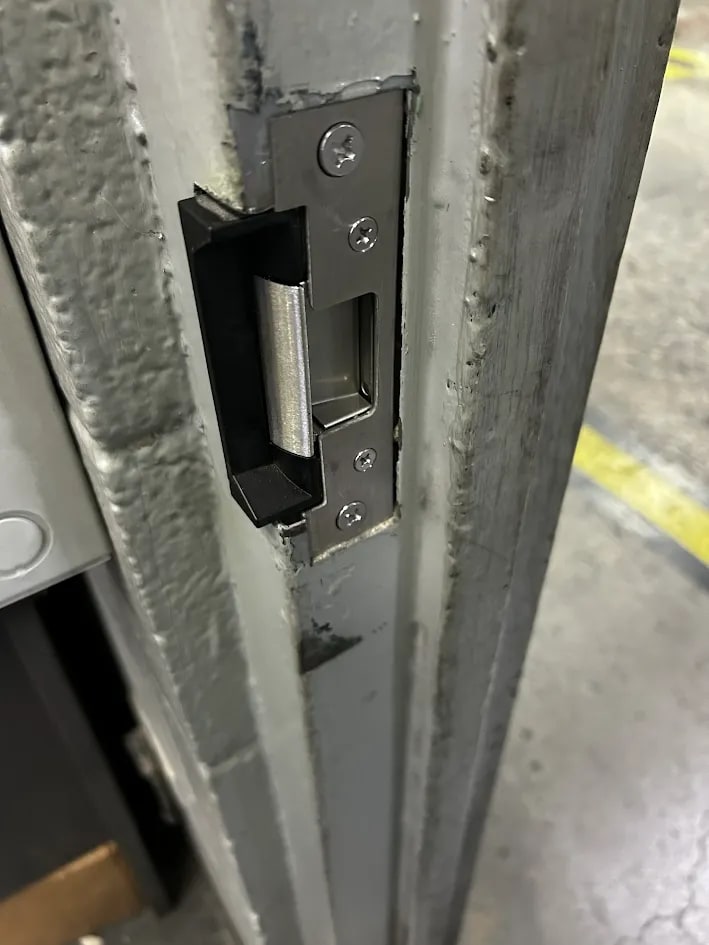 Brushed steel electric strike set into the grey steel door frame with a curved keeper and four screws