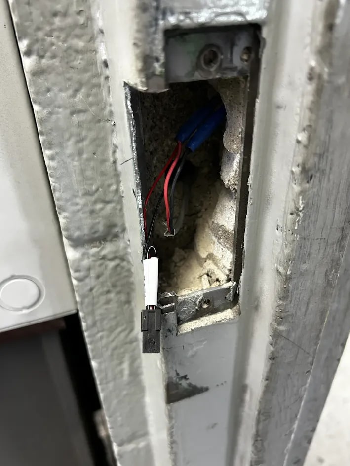 Closer view of the door frame cutout showing red and black wiring and a white inline connector against roughened steel