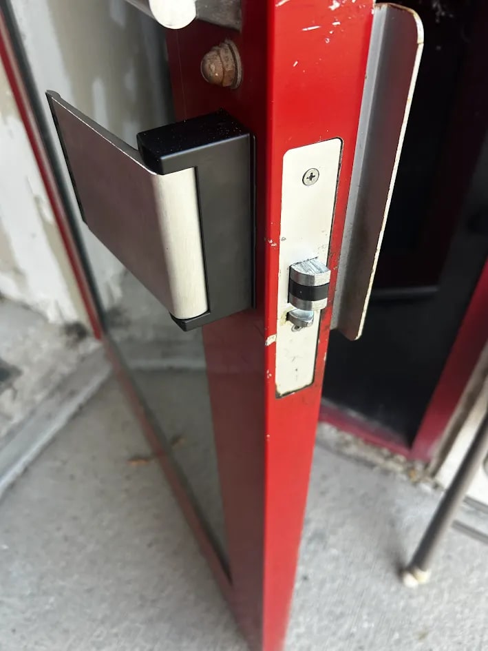 Black-backed paddle assembly and a steel latch faceplate with a cam fitted to the edge of a red-framed glass door