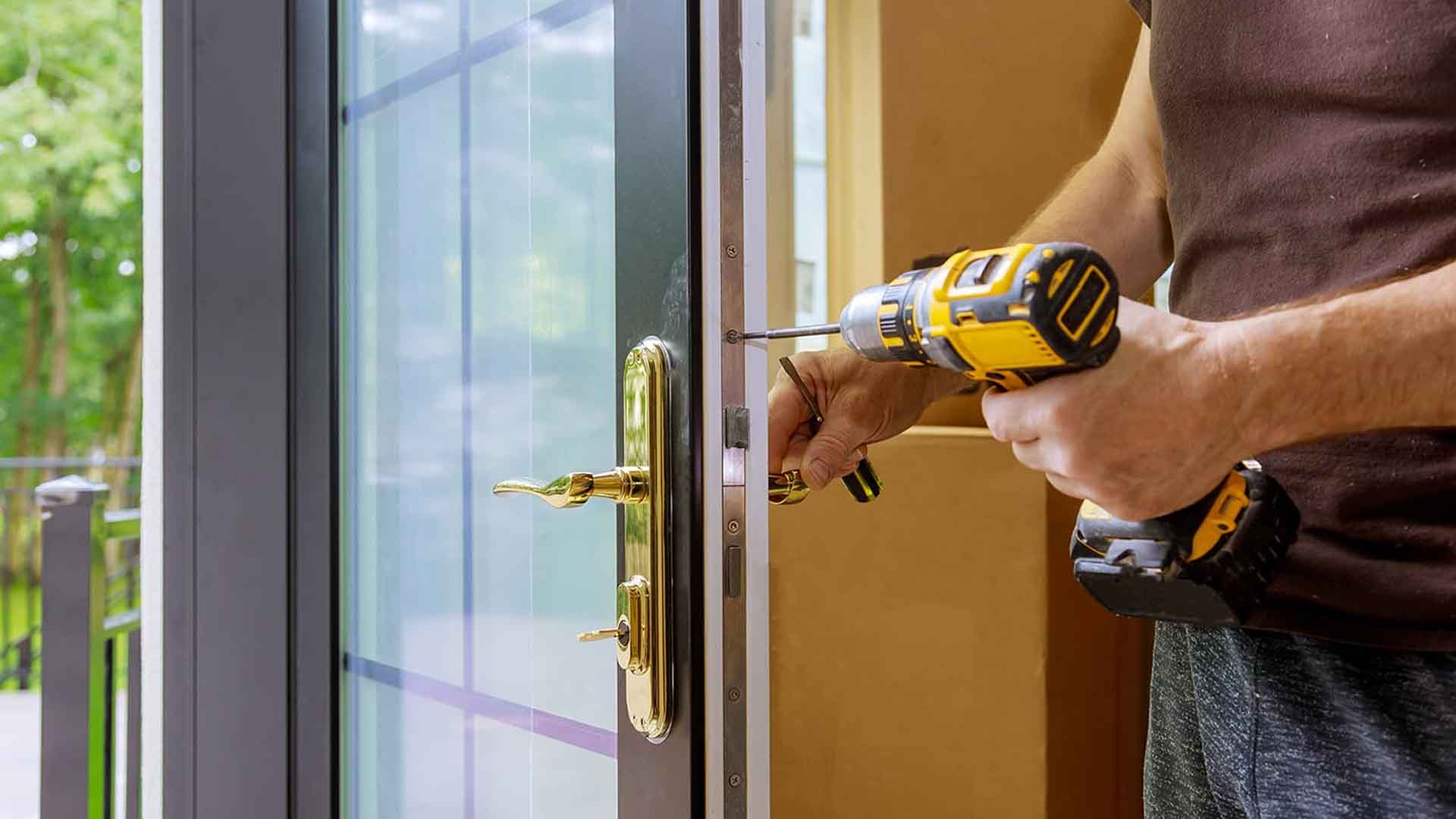 Man using a cordless drill beside a brass lever handle on glass door