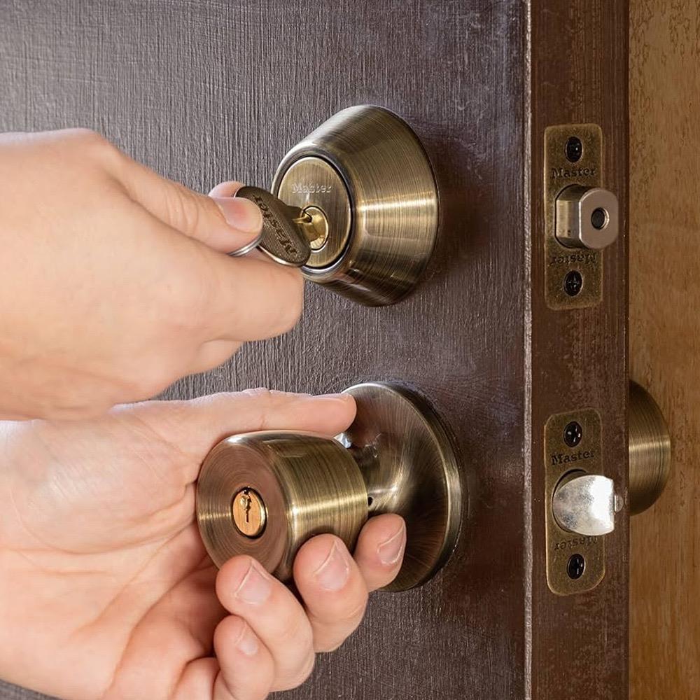 Hands inserting a key into a brass deadbolt on a dark wood door
