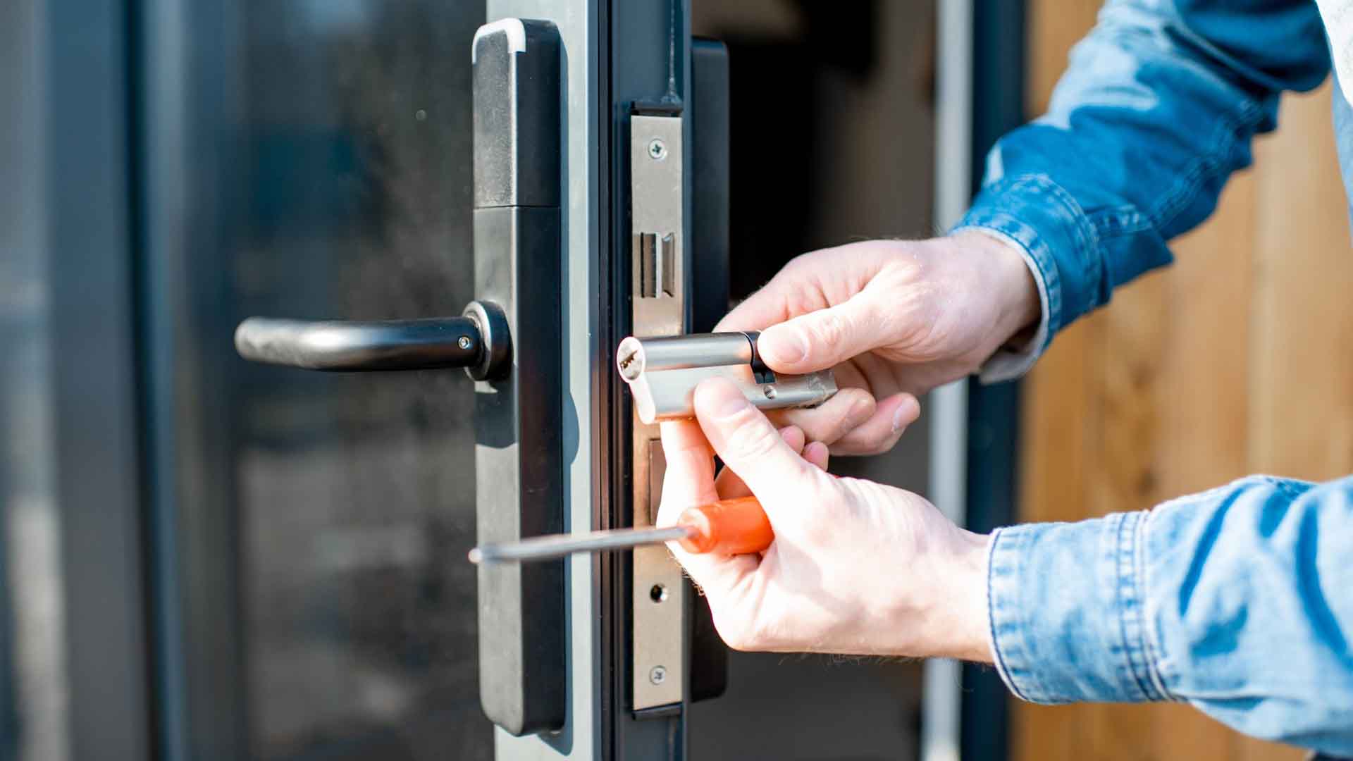Person in denim jacket using a screwdriver to install a door lock cylinder