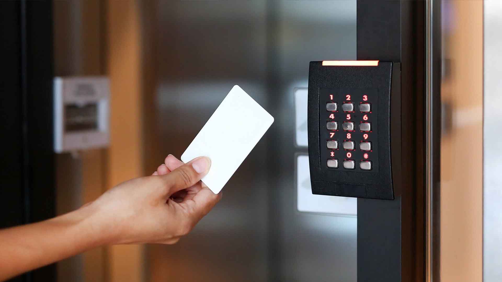 Hand holding a white access card beside a black keypad reader on glass door