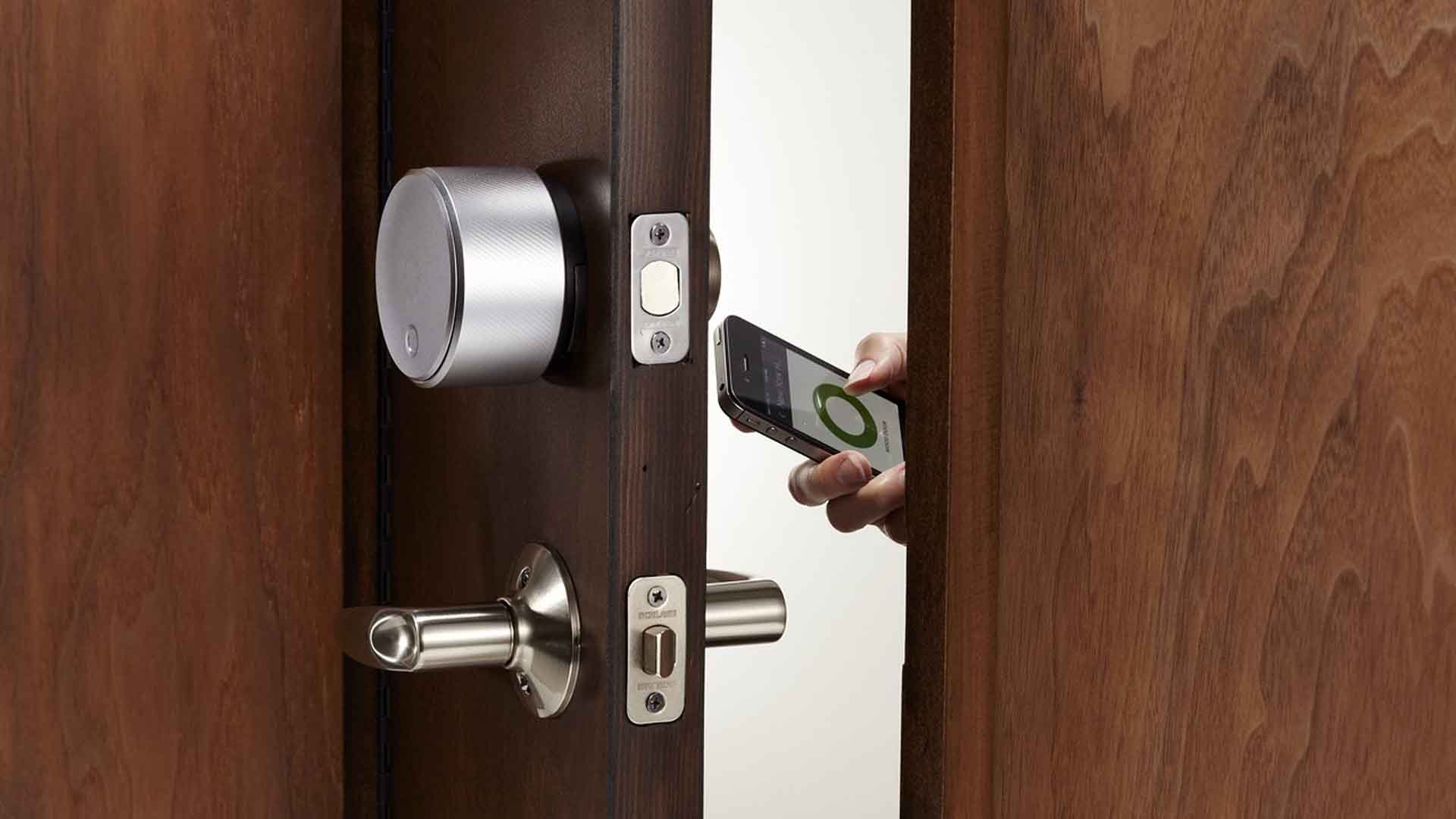 Hand with a smartphone app next to a silver smart lock on wood door
