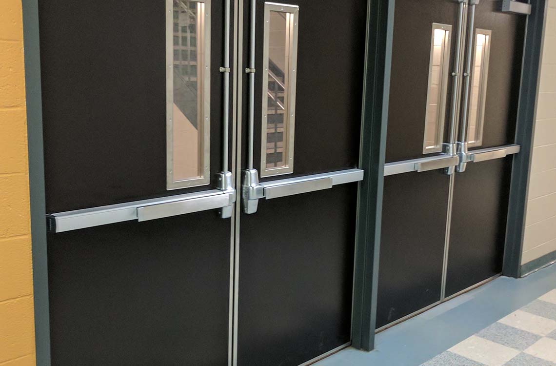 Black commercial double doors with metal push bars and narrow vertical windows